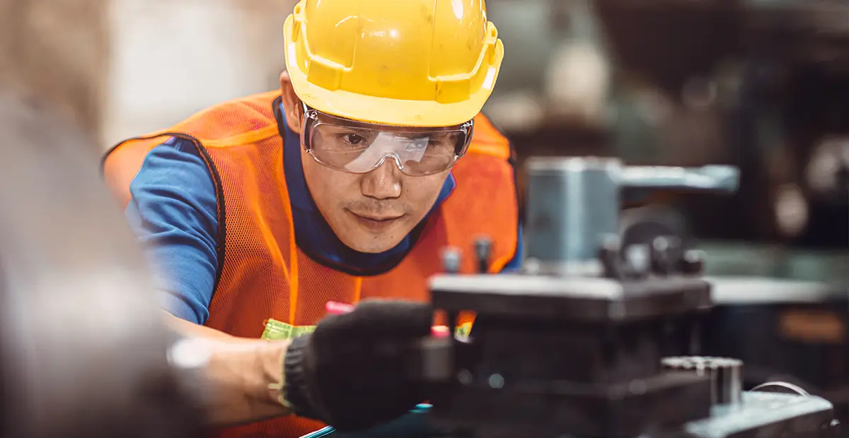 Man with yellow hard hat and safety goggles inspecting machinery