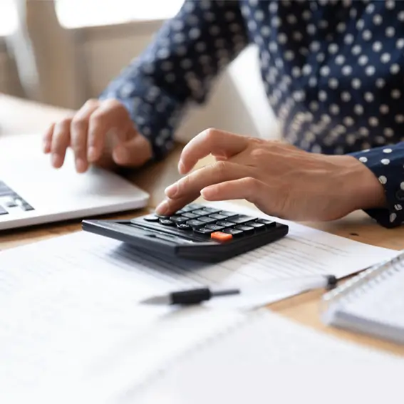 Person using calculator with left hand while using laptop with right