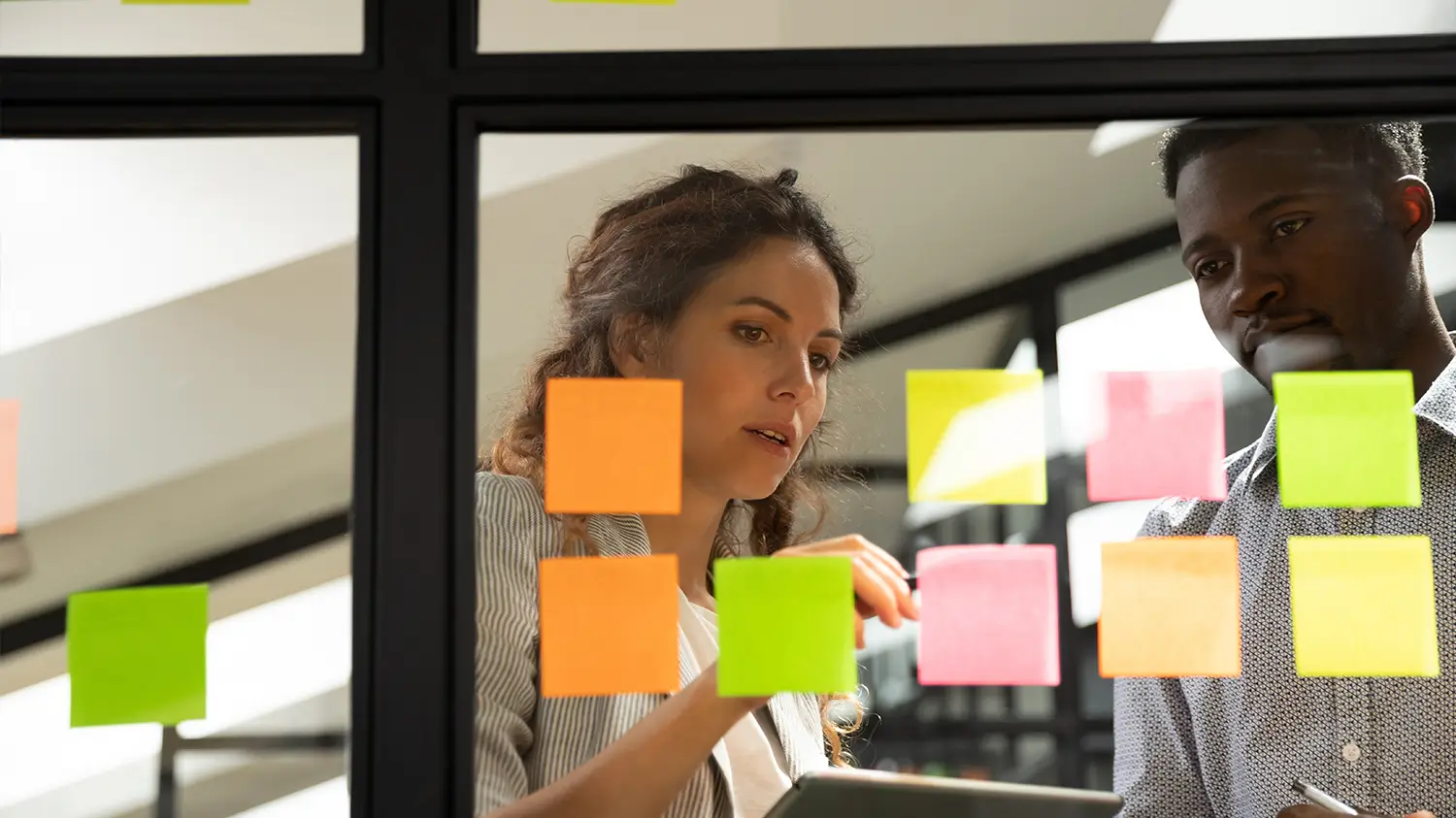 Man and woman putting sticky notes on a pane of glass