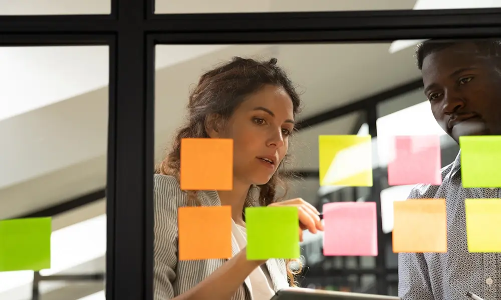 Man and woman looking at sticky notes on pane of glass